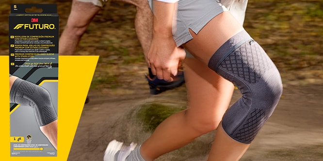 Corredor en un sendero que lleva una manga de compresión premium para rodilla FUTURO, con el embalaje del producto visible
